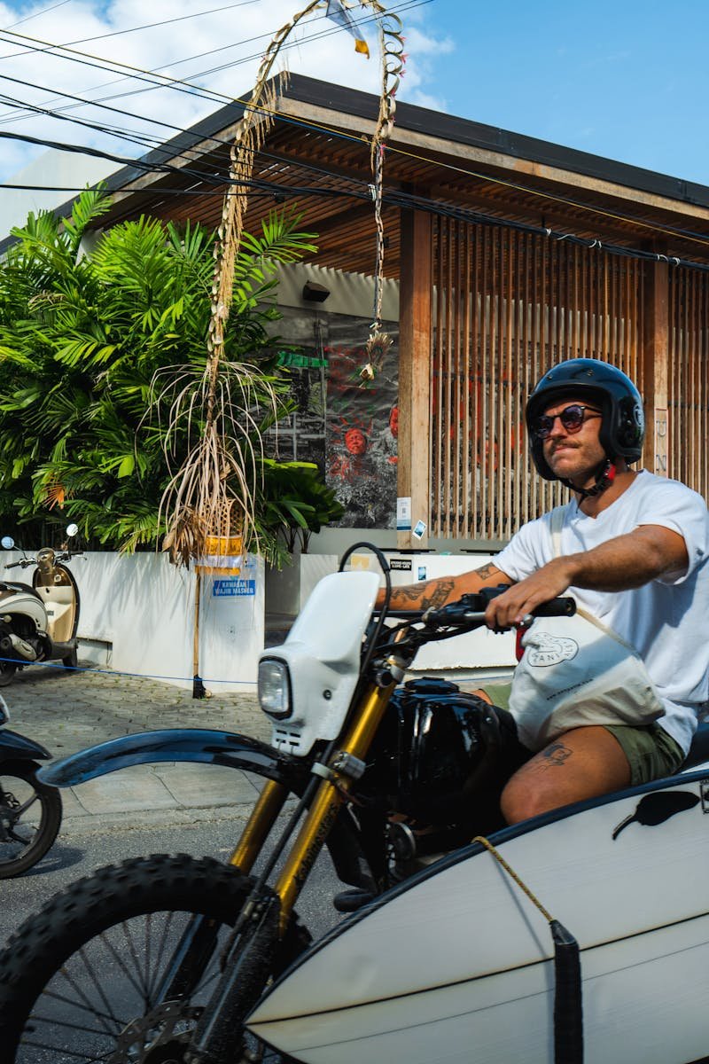 Man riding a motorbike with a surfboard in Bali, Indonesia. Street scene with tropical ambiance.