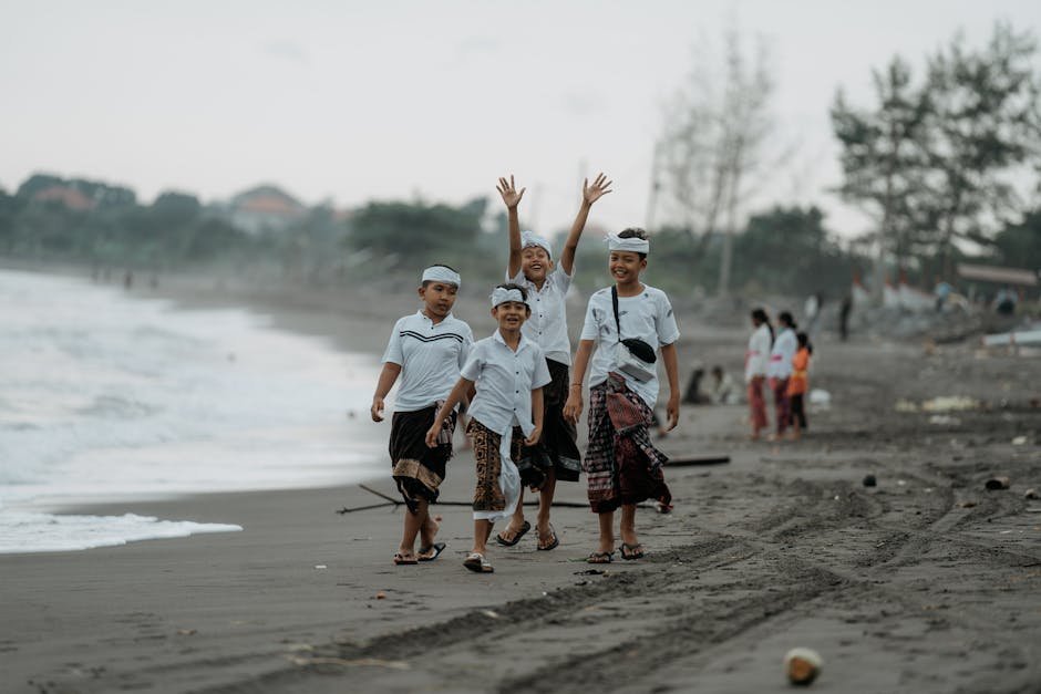 Group of children walking joyfully along Sanur Beach wearing traditional attire. Lively and cultural scene.